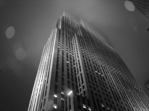Tiro de ângulo baixo de um edifício de cidade alto em uma névoa em preto e branco — Fotografia de Stock