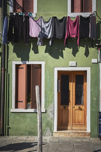 A green building with wooden doors and windows and colorful clothes hanging on the cable in Burano — 스톡 사진