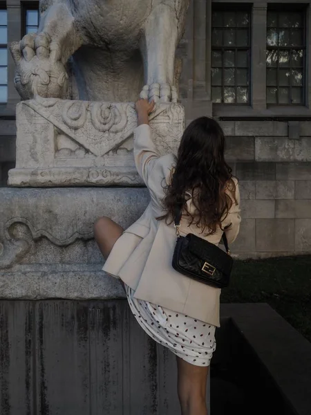 Вертикальный снимок женщины в белой куртке и черной сумке, пытающейся забраться на каменную скульптуру — стоковое фото