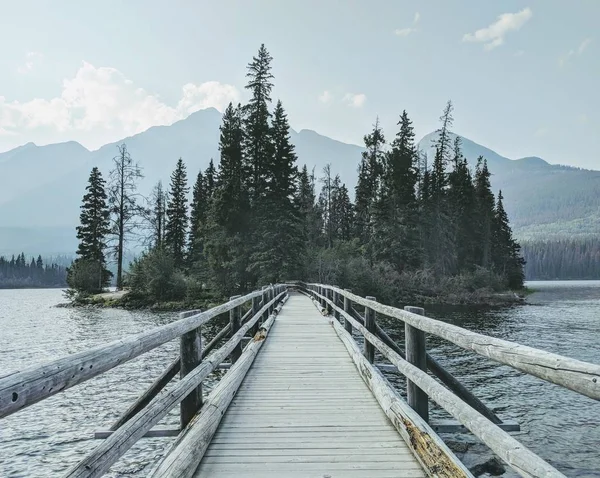 Beautiful shot of a wooden bridge over the water towards the forest with mountains in background — Stock Photo, Image