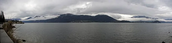 Tiro panorâmico de um mar com montanhas na distância abaixo de um céu nublado — Fotografia de Stock