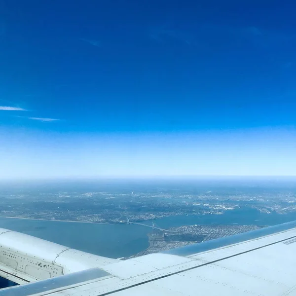Vista aérea de un paisaje desde una ventana plana con el océano y edificios altos bajo el cielo azul — Foto de Stock