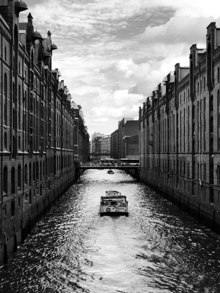 Grayscale tiro vertical de um barco no corpo de água entre os edifícios — Fotografia de Stock