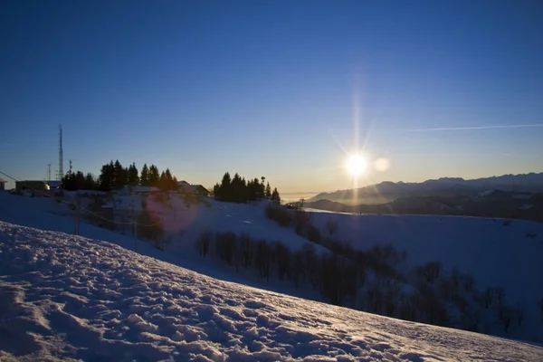 Belo tiro de montanhas nevadas com o sol brilhando em um céu azul claro no fundo — Fotografia de Stock
