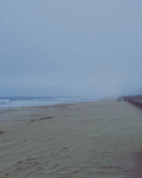 Vertikale Aufnahme des wunderschönen welligen Meeres und des leeren Strandes, der am frühen Morgen in Nebel gehüllt ist — Stockfoto