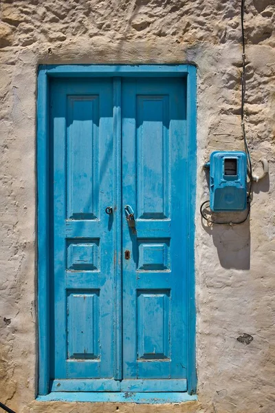 Tiro vertical de uma porta de madeira azul em uma parede velha durante o dia em Symi, Grécia — Fotografia de Stock