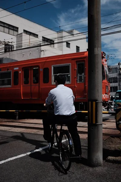 흰색 셔츠를 입고 빨간 버스 근처의 거리에서 자전거를 타고 있는 남성의 수직 사격 — 스톡 사진