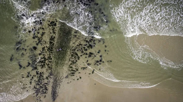 Tiro de ângulo alto da praia com um monte de pedras perto das ondas do oceano — Fotografia de Stock