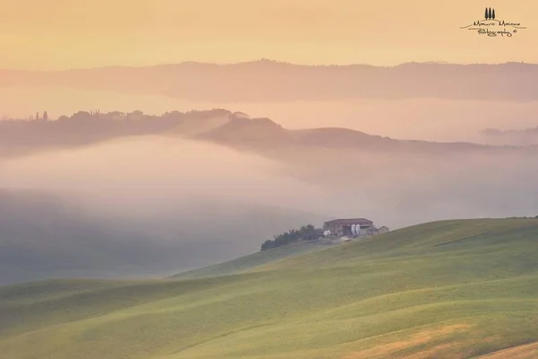 Aufnahme eines Hauses auf einem grasbewachsenen Hügel mit Bergen im Nebel im Hintergrund — Stockfoto