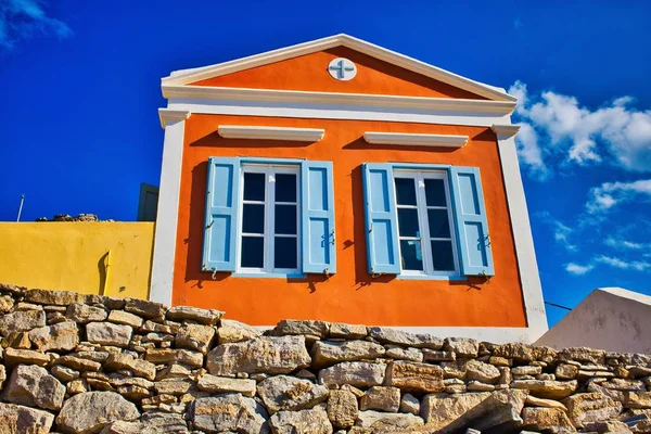 Снимок оранжевого дома с голубыми окнами на фоне голубого облачного неба в Греции — стоковое фото