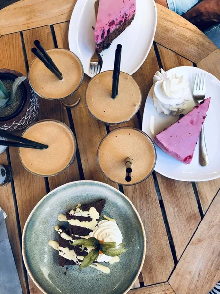 Tiro aéreo vertical de xícaras de café perto de chapas com bolos de queijo e sobremesas em uma mesa de madeira — Fotografia de Stock