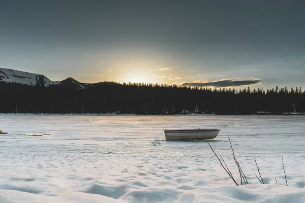 Amplio plano de un barco en un lago congelado rodeado de siluetas de árboles — Foto de Stock