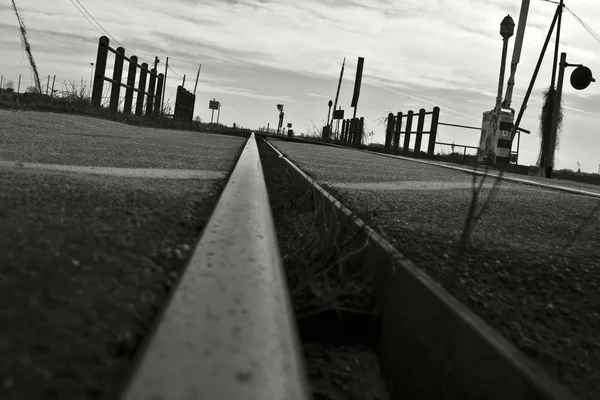 Niski kąt strzału toru kolejowego pod zachmurzonym niebem w czerni i bieli — Zdjęcie stockowe