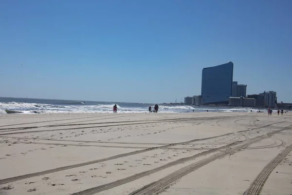 Beautiful shot of people walking on the beach shore with buildings in the distance — Stock Photo, Image