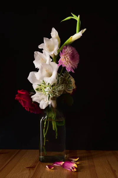 Вертикальний знімок різних квітів у банці на дерев'яній поверхні з чорним тлом — стокове фото