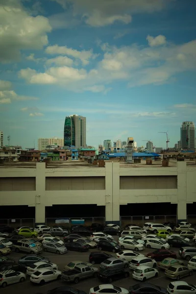 Colpo verticale di veicoli parcheggiati in un parcheggio vicino a edifici sotto un cielo nuvoloso blu — Foto Stock