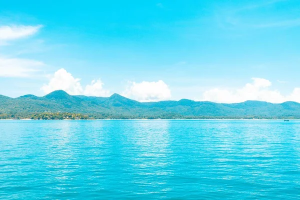 Belo tiro do mar de água azul com montanhas arborizadas na distância abaixo de um céu azul — Fotografia de Stock