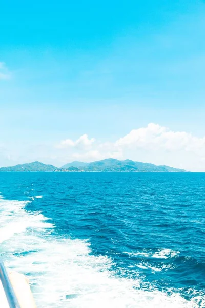 Tiro vertical de um barco no mar com montanhas na distância abaixo de um céu azul — Fotografia de Stock