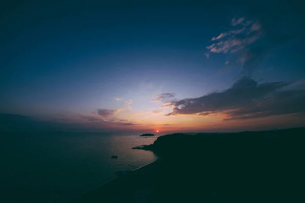 Foto aerea della riva vicino all'acqua sotto un cielo blu con il sole che tramonta sullo sfondo — Foto Stock