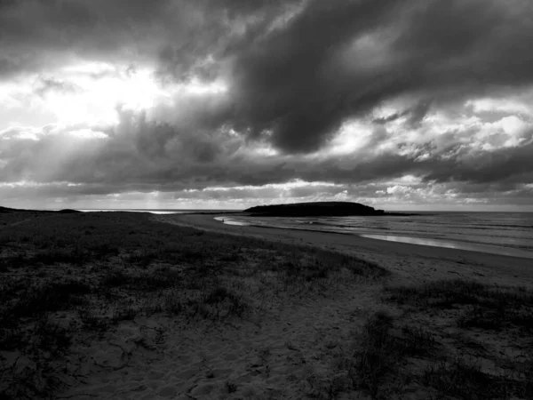 Beautiful shot of the beach shore under a cloudy sky in black and white — Stock Photo, Image