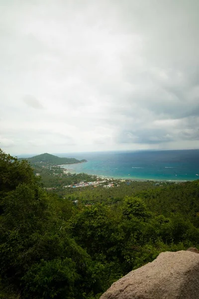 Vertikale Aufnahme von Hügeln mit Bäumen in der Nähe des Meeres unter wolkenverhangenem Himmel — Stockfoto