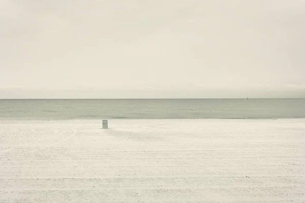 Apacible orilla arenosa del mar tranquilo con un solo barril en la arena bajo el cielo blanco puro —  Fotos de Stock