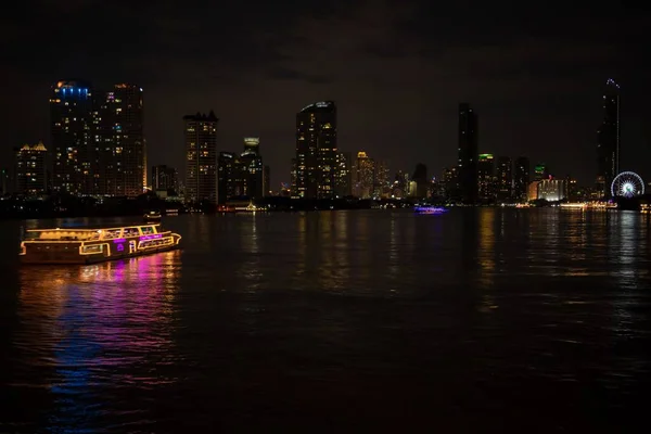 Wide shot of a lighted boat on the body of water surrounded by skyscrapers during nighttime — Stock Photo, Image