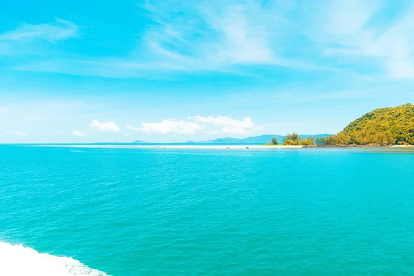 Belo tiro do mar com uma colina coberta de árvores sob um céu azul durante o dia — Fotografia de Stock