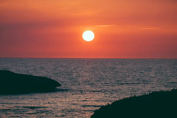 Silueta de orillas cerca del agua con el sol en un cielo naranja en el fondo — Foto de Stock