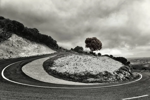 Scatto in scala di grigi di una curva a U tagliente sulla strada di campagna — Foto Stock