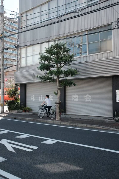 Вертикальный снимок человека, едущего на велосипеде по тротуару возле дерева и здания на улице — стоковое фото
