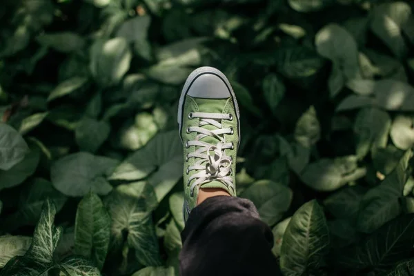 Shallow colpo focalizzato del piede di una persona che indossa una sneaker verde con una punta bianca e lacci — Foto Stock