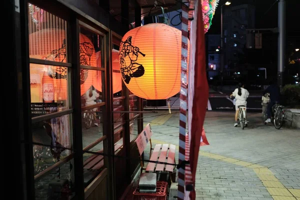 Gros plan sélectif d'une lanterne en papier orange clair près de fenêtres en verre pendant la nuit — Photo