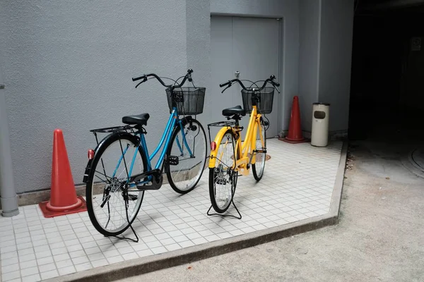 Wide shot of blue and yellow bicycles with baskets on a pavement near gray walls — Stock Photo, Image
