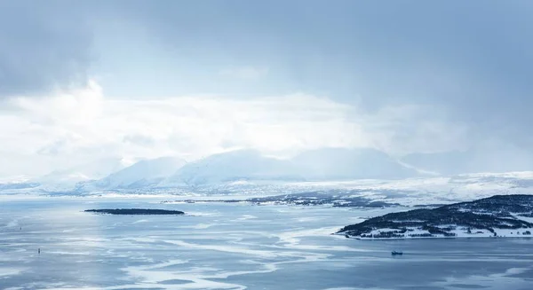 Vodorovný záběr vodní plochy pokryté ledem obklopeným horami pod bílými mraky — Stock fotografie