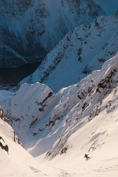 Tiro vertical de alta cordilheira coberta de neve e uma pessoa esquiando durante o dia — Fotografia de Stock