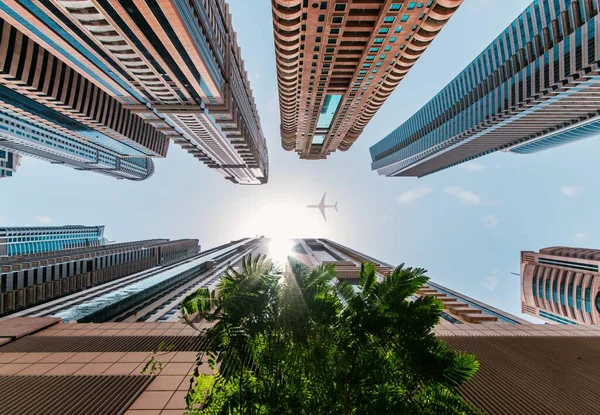 Tiro de ângulo baixo de arranha-céus de edifício alto e um avião abaixo dos raios de sol brilhantes — Fotografia de Stock