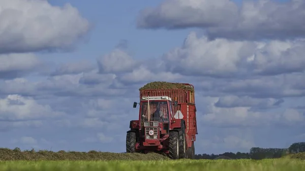 Tractor rojo conduciendo en un campo agrícola con un cielo azul nublado en el fondo —  Fotos de Stock