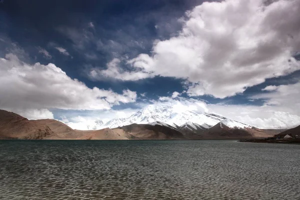 Poziome ujęcie jeziora Karakol otoczone wysokimi górami pokrytymi śniegiem w Chinach — Zdjęcie stockowe