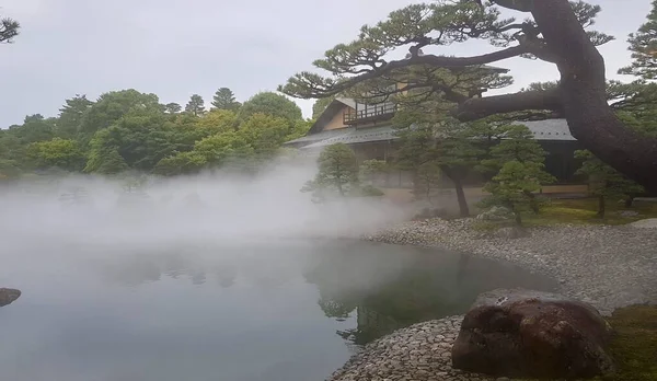 Beautiful shot of a house near the water and trees in a fog — 스톡 사진