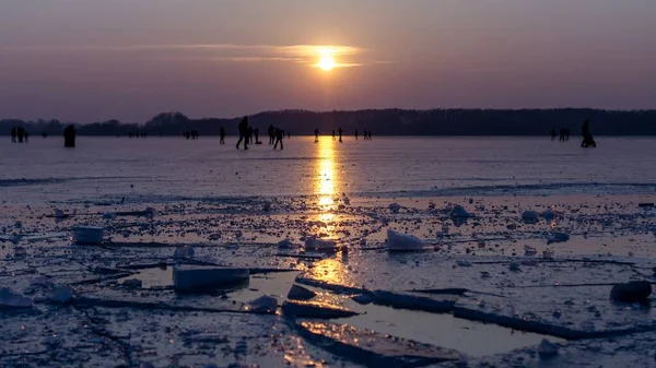 Paisaje de hielo agrietado en un cuerpo congelado de agua con personas jugando a la distancia — Foto de Stock