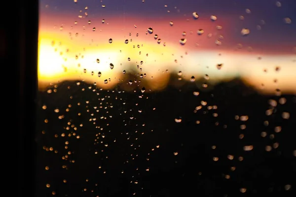 Tiro de close-up seletivo de gotas de água em uma janela de vidro no fundo embaçado do pôr do sol — Fotografia de Stock
