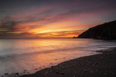 Breathtaking sunset over the calm ocean in Polkerris, Cornwall, UK clipart