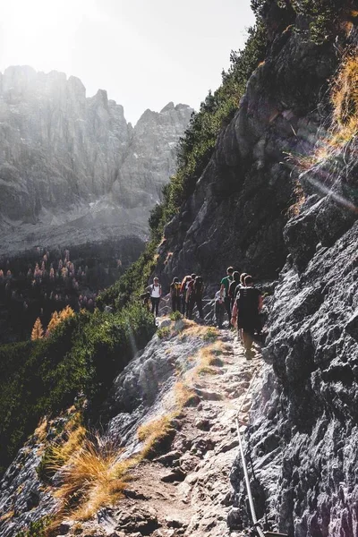 A vertical shot of people walking on the side of the mountain at daytime shot from behind