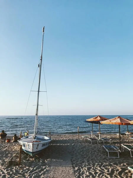 Tiro vertical de un velero blanco en la orilla cerca del agua con un cielo azul en el fondo —  Fotos de Stock