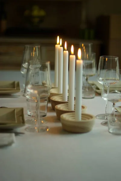 Tiro vertical de cinco velas brancas acesas em uma mesa com copos de vinho e talheres — Fotografia de Stock