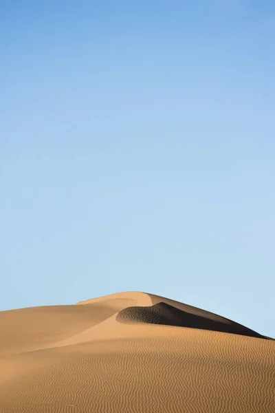 Verticale opname van zandduinen in een woestijn met de blauwe lucht in de rug gedurende de dag — Stockfoto