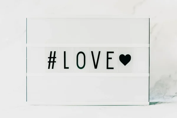 Primer plano horizontal de un papel blanco con una impresión # LOVE sobre un fondo blanco —  Fotos de Stock