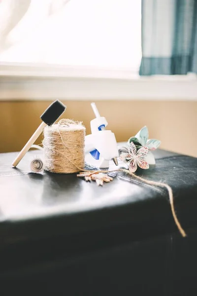 Gros plan vertical d'un fil de paille, d'un pistolet à colle et de fleurs en papier sur un tuffet noir — Photo