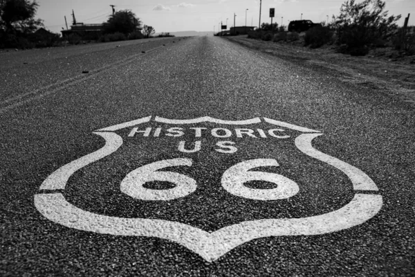 Горизонтальный снимок в серой шкале знака "Исторический US 66" на улице Route 66 в окружении деревьев — стоковое фото